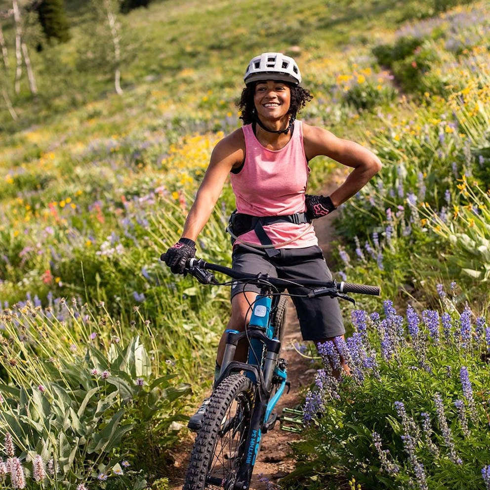 Emilé Newman sitting on her mountain bike on a singletrack trail surrounded by flowers