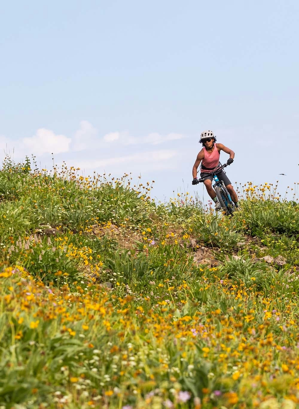 Emilé Newman riding her mountain bike on a singletrack trail surrounded by flowers