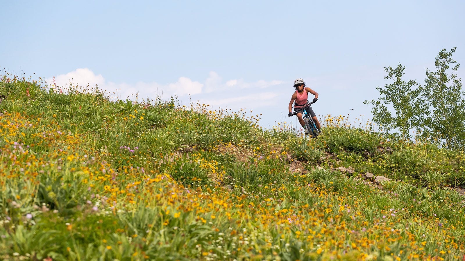 Emilé Newman riding her mountain bike on a singletrack trail surrounded by flowers