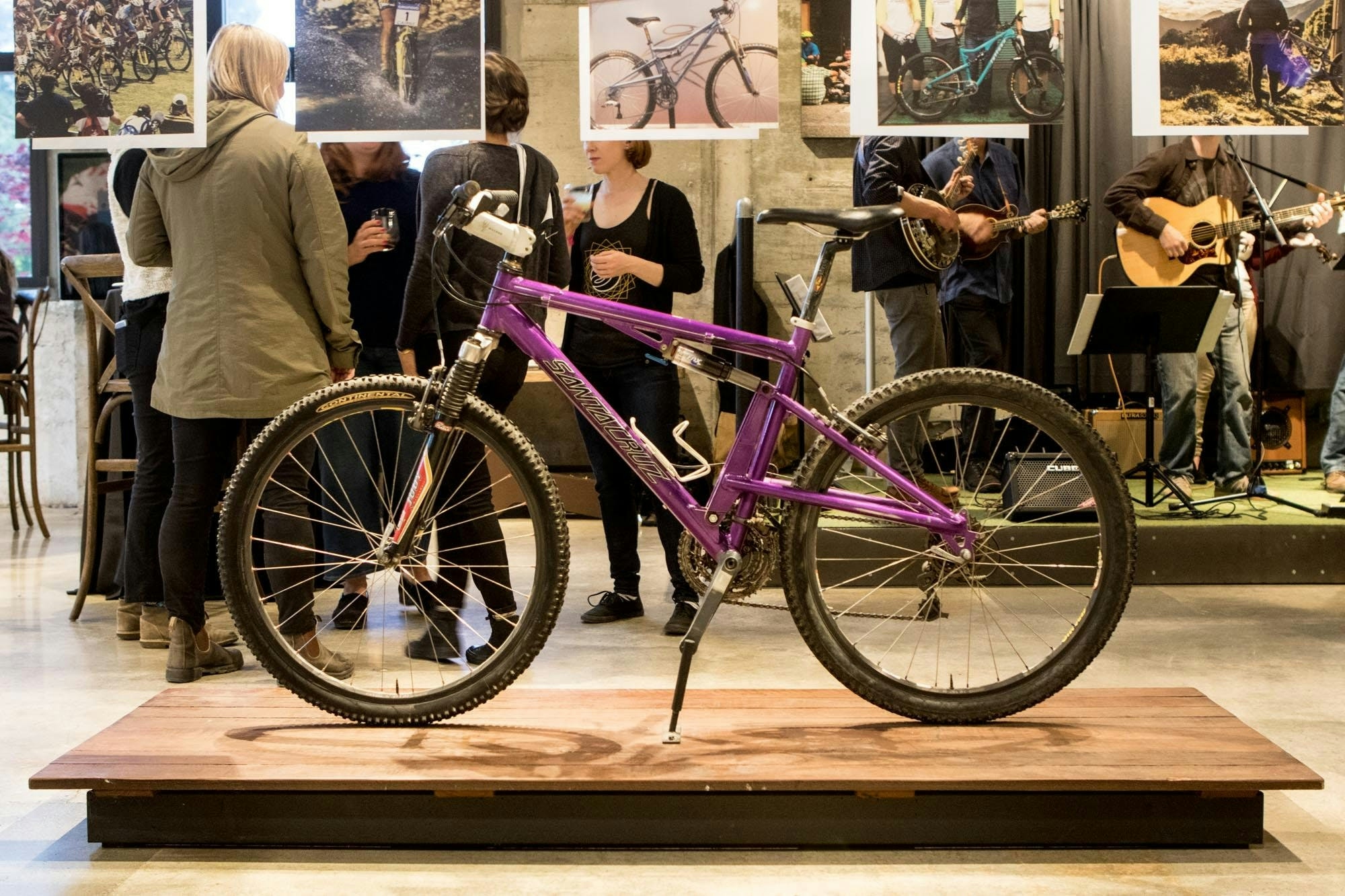 An older Santa Cruz Mountain Bike - Purple frame on a wood platform in a showroom with people in the background