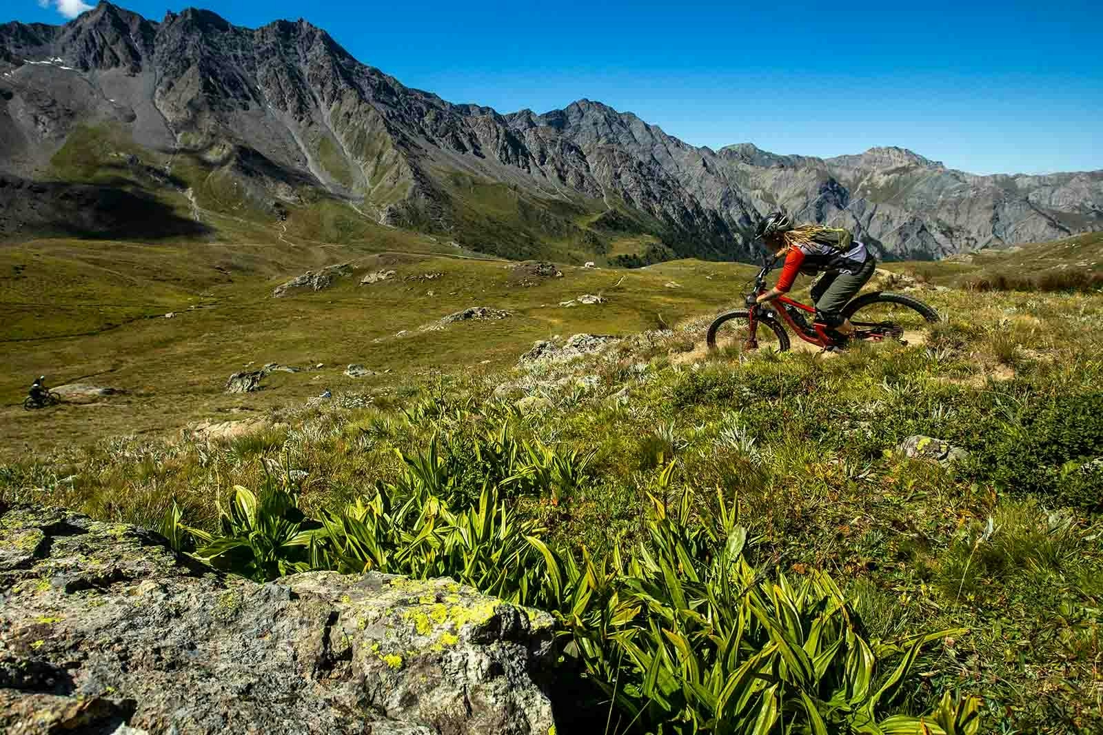 Anka Martin riding her mountain bike through a field with mountains in the background